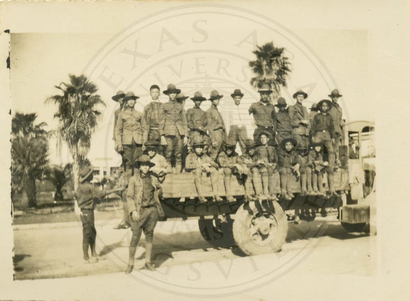Men riding the bed of the school truck.
