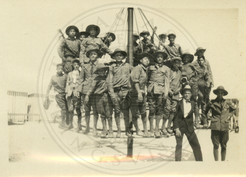 Boys on top of a circular bar, two men beside them.