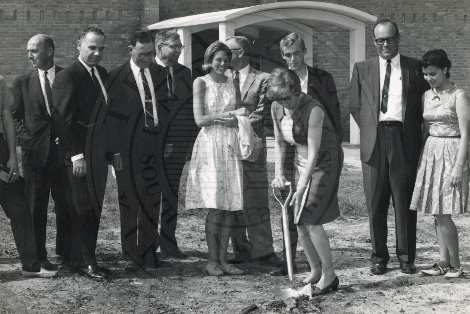 Groundbreaking: a woman with the shovel, everyone in formal dress.