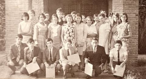 The Class of 1972 as underclassmen, posed against a brick wall with their certificates.