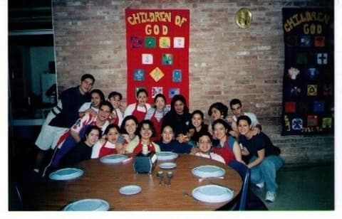 The kitchen crew around a dining-hall table under the “Children of God” banners, late 1990s.