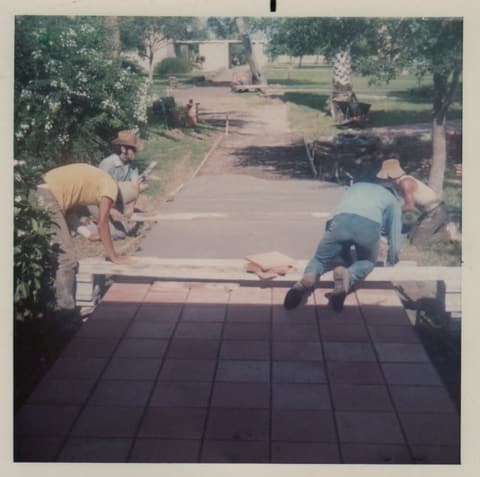 Students on their knees laying the brick walkway; commenters think Eddie and Miguel Plana are among them.