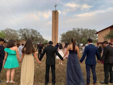 Students in formal wear holding hands in a circle around the chapel tower.
