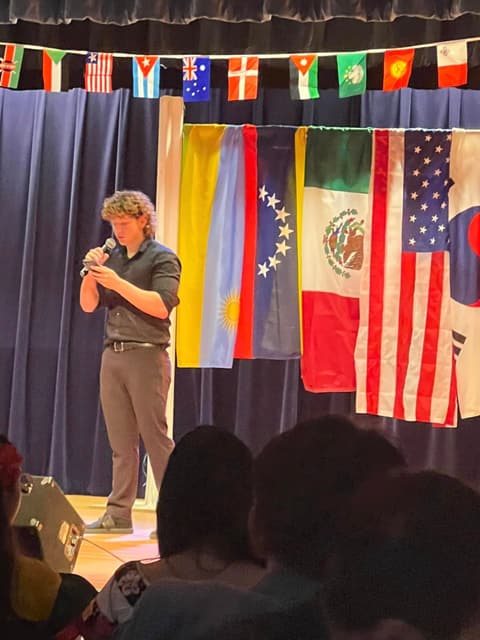 A student recites a T. S. Eliot poem on stage at the International Banquet, March 2024, under the flags of students’ home countries.