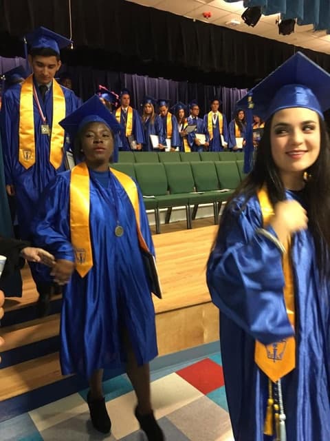 New graduates walking off the stage, one adjusting her cap.