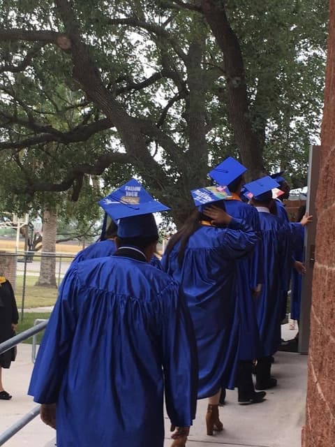 Graduates with decorated caps heading in under the oaks.