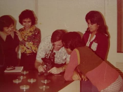 Students crowd around a teacher at the microscope in the science lab.