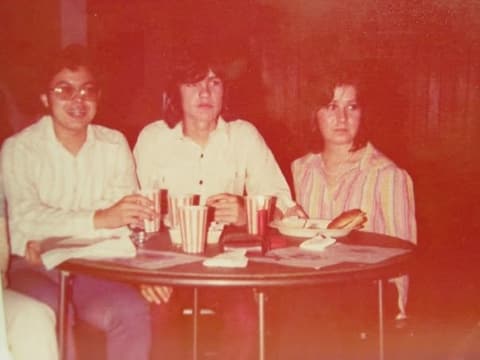 Three friends at a dinner table; a commenter remembers Belinda as ‘so sweet’.