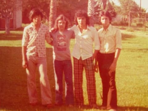 Four friends in bell-bottoms and plaid on the lawn under the palms.