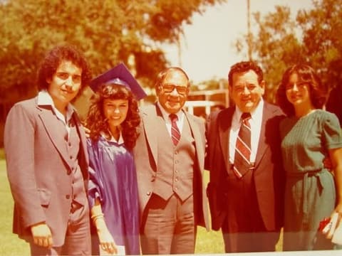 A graduate with her family and a teacher on graduation day; a commenter remembers Mr. Leos as ‘a great person’.