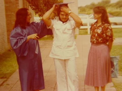 A classmate tries on a graduate’s mortarboard on the walkway on graduation day; Bianka Arredondo recognizes Judith, her first roommate.