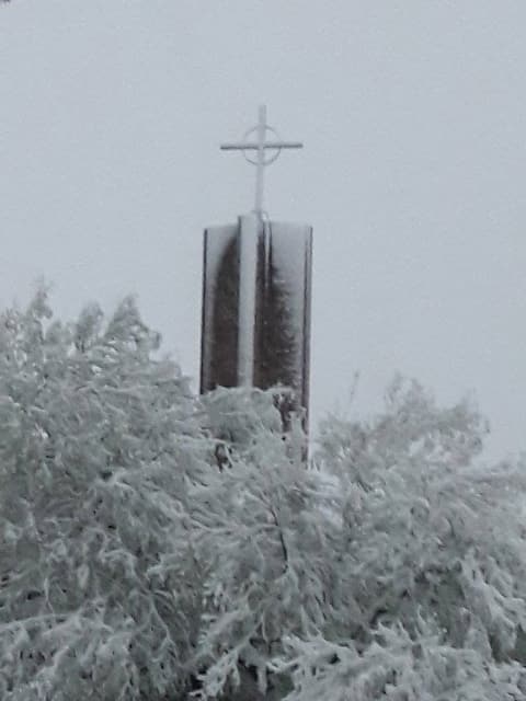The chapel tower and its cross above snow-covered trees, December 8, 2017.