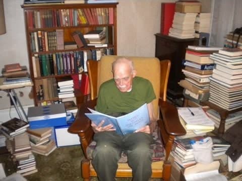 Mr. Perry Reed reading in his armchair among his books; alumni remember he was never without one.