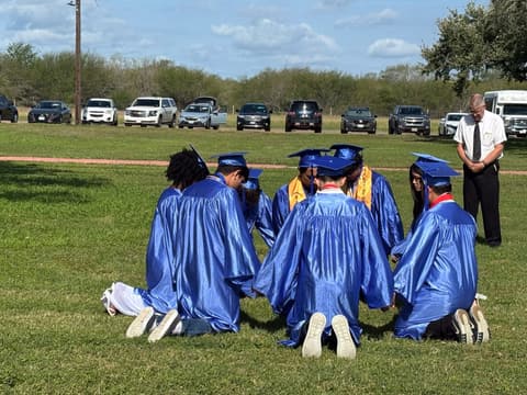 The Class of 2026 kneeling in a circle on the lawn after graduation.