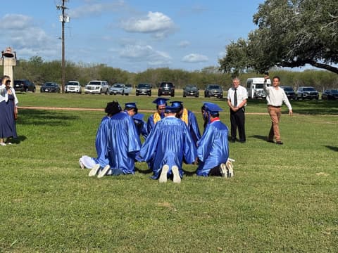 The Class of 2026 kneels in a circle on the lawn after graduation, a tradition begun by the Class of 1999.