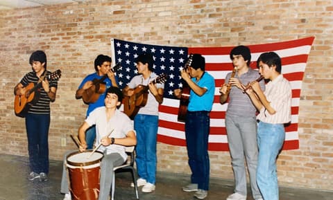 The Grupo Folklórico, known as “Los Panchos”, with guitars, flutes and a drum in front of the flag; commenters name Othoniel, Josué, Raúl Miranda, David Monterrey, Omero Ornelas, Franky Perales, Hugo Rocha and Tony Gonzalez.
