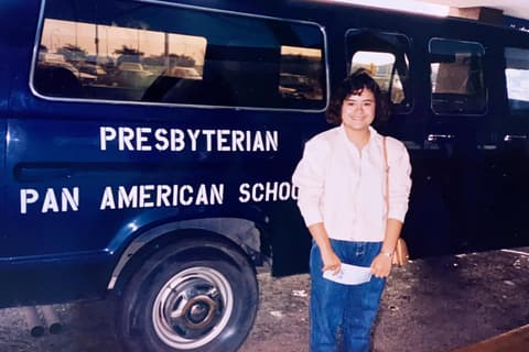 A student beside the school’s navy “Presbyterian Pan American School” van; a classmate recognizes her.