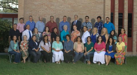 The faculty and staff of Presbyterian Pan American School in front of a campus building.