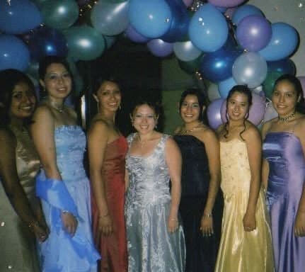 Seven students in formal dresses in front of blue and silver balloons, at a banquet.