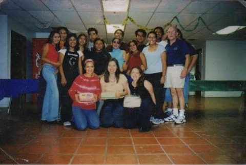 Students gathered around a staff member at an indoor celebration, some holding cake boxes.