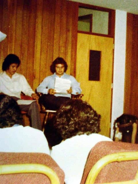 Students reading at a program in a wood-paneled hall.