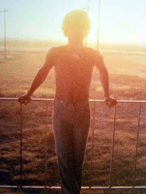 A student silhouetted against the sunset at the fence.