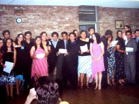 Students in their best clothes holding certificates at an awards night in the dorm lounge.