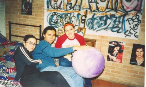 Roommates in their dorm room, under a graffiti banner and posters of their favourite singers.