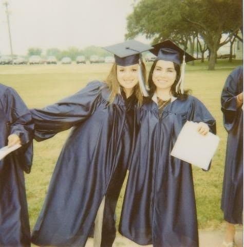 Two graduates in caps and gowns on the lawn on graduation day.