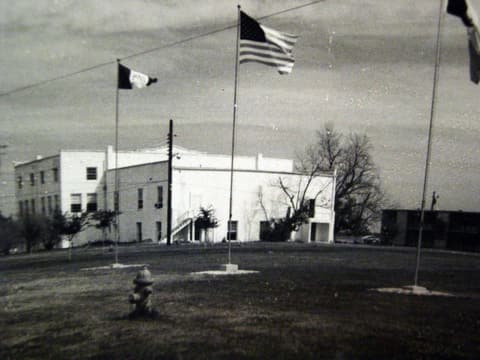 An early campus building under the flags, in an old photograph.