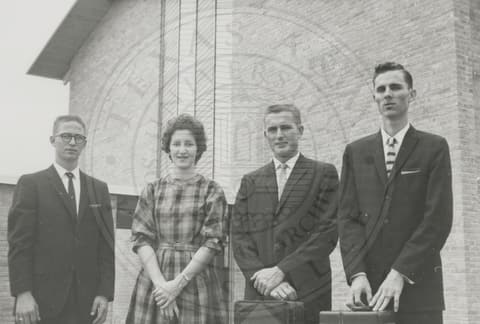 Three men in suits and woman.