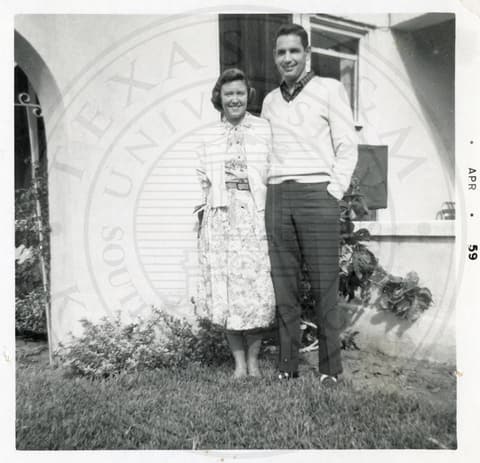A man and a woman standing next to each other on grass outside a building.
