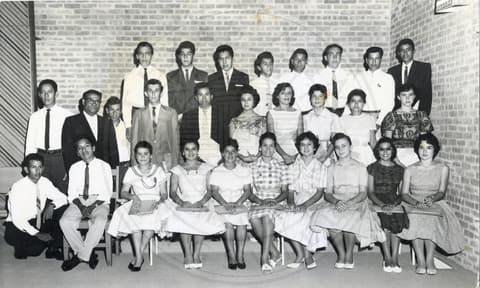 Students. Students dressed in formal. They are standing in three rows with the students in the first row sitting on chairs.