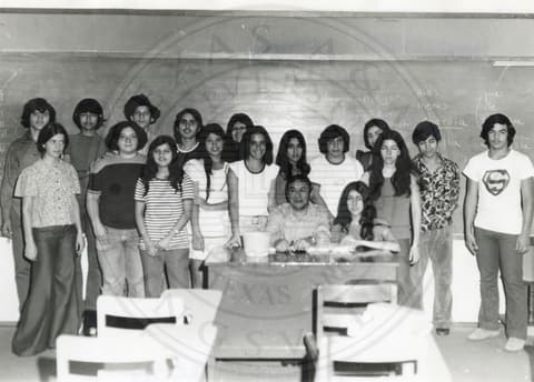 Teacher & Students. Students standing in a group with their teacher sitting in the center in a classroom.